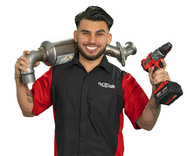 a smiling mechanic holds a catalytic converter on his shoulder and a cordless drill in his other hand, wearing a Red McCombs Automotive Group uniform