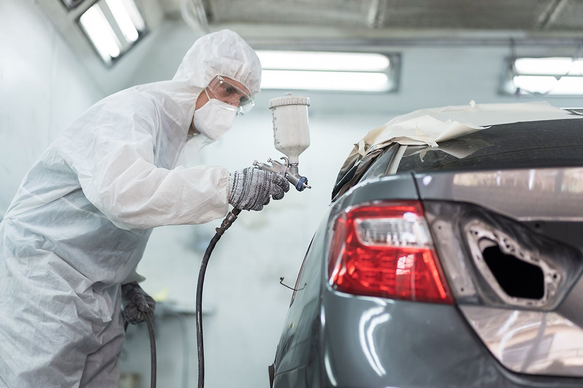 auto technician spray painting a car in a professional paint booth